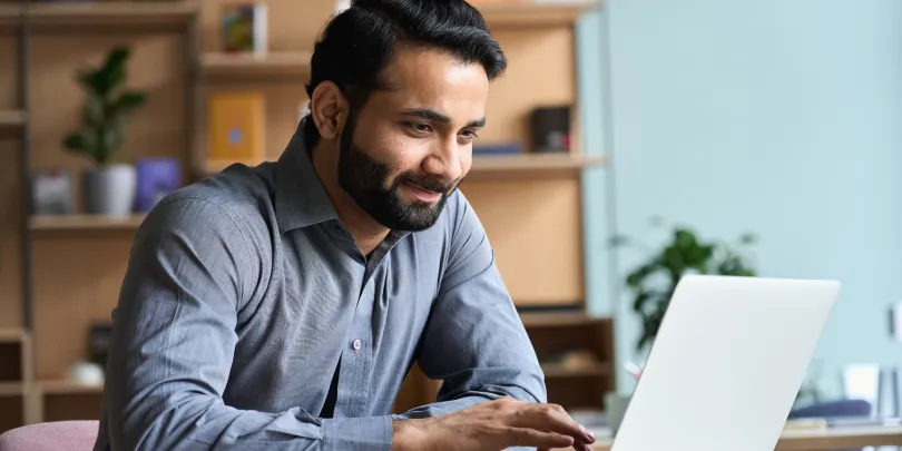 A focused man at his desk reviewing data on a laptop about automated campaign optimization.